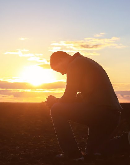 Man praying outdoors at sunset