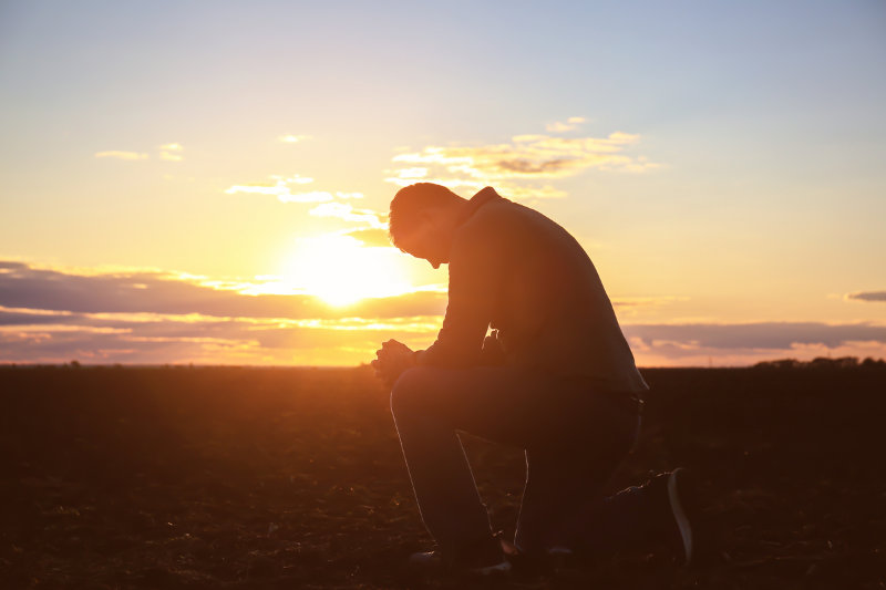 Man praying outdoors at sunset