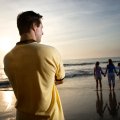 Father standing on an ocean beach at sunset watching children